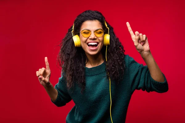 Foto van vrolijke mooie donkere huid jonge dame goed humeur dragen headset zonneglas dans geïsoleerd op rode kleur achtergrond — Stockfoto