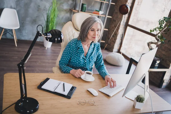Fotografie staré ženy šťastný pozitivní úsměv sedět kancelář stůl pohled číst procházet počítač přestávka pauza zbytek pít horkou kávu — Stock fotografie