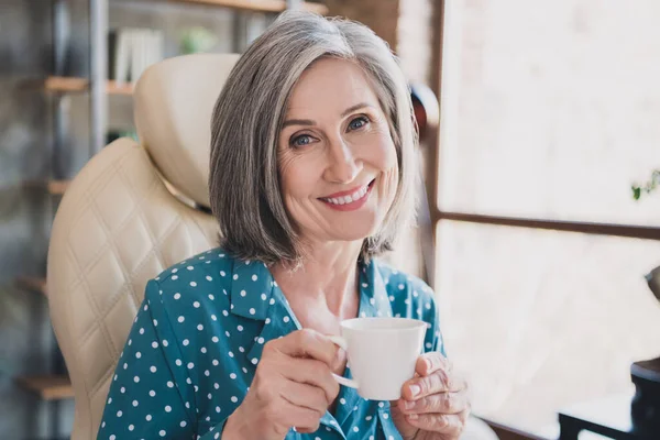 Foto van vrolijke oude vrouw gelukkig positieve glimlach ontspannen pauze drinken hete koffie thee genieten binnen — Stockfoto