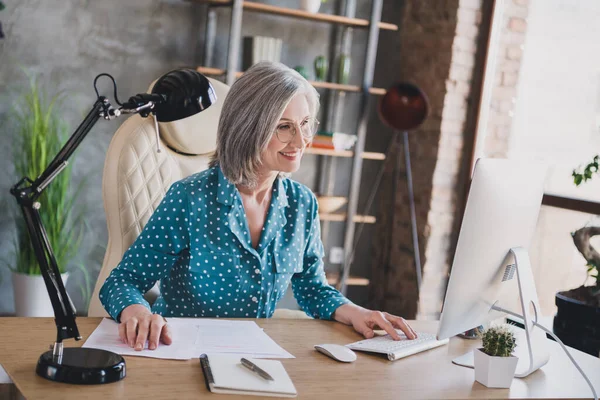 幸せな魅力的な老女ビジネスの女性の写真は、室内オフィスの職場でコンピュータの笑顔リモートワークを見て — ストック写真