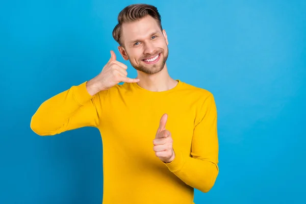긍정적 인 미소를 짓고 있는 젊은 남자의 사진은 당신 이 파란색 배경으로 고립되어 있는 손가락을 가리키는 전화 신호를 보여준다 — 스톡 사진