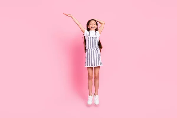 Plná délka fotografie šťastný pěkný hezká dívka skok nahoru držet ruku prázdný prostor opatření izolované na růžové barvy pozadí — Stock fotografie