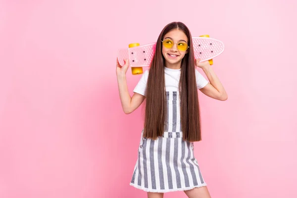 Fotografie šťastné pěkné atraktivní roztomilé holčička držet longboard vzhled prázdný prostor úsměv izolované na růžové barvy pozadí — Stock fotografie