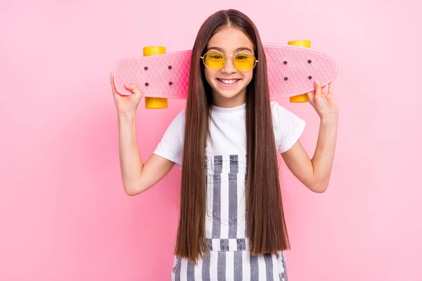 Foto van schattige schattige kleine meisje houden longboard achter hoofd glimlach goed humeur geïsoleerd op roze kleur achtergrond — Stockfoto