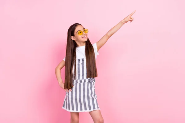 Fotografie veselý šťastný pěkný holčička vzhled ukazováček prázdný prostor oblečení sluneční sklo izolované na růžové barevné pozadí — Stock fotografie