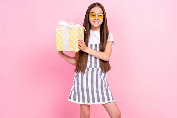 Φωτογραφία πορτρέτο της μικρής μαθήτριας σε συνολικά γυαλιά χαμογελώντας διατηρώντας το παρόν κουτί απομονωμένο παστέλ ροζ χρώμα φόντο — Φωτογραφία Αρχείου