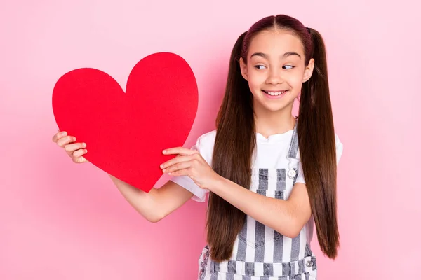 Foto retrato de menina com caudas sorrindo mostrando cartão postal coração vermelho isolado no fundo cor-de-rosa pastel — Fotografia de Stock