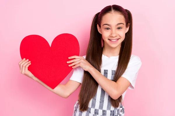 Foto de alegre agradável positivo pequena menina bom humor segurar vermelho papel coração isolado no fundo cor-de-rosa — Fotografia de Stock