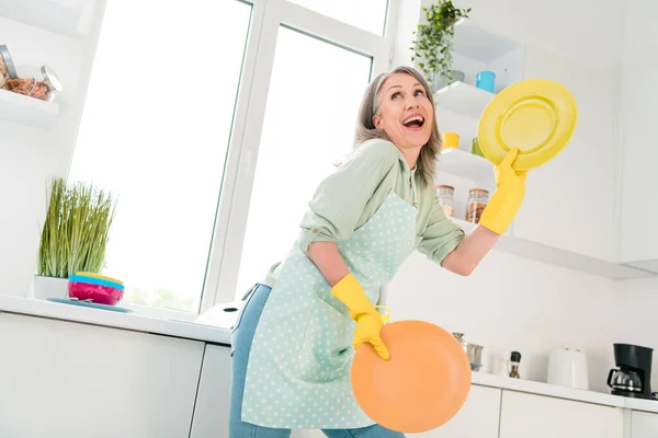 Portret van een aantrekkelijke vrolijke grijsharige vrouw die afwas doet dansen snel gemakkelijk service netjes opruimen thuis licht wit binnen — Stockfoto