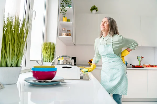 Портрет привабливої хворої сіро-волохатої жінки, яка робить посуд обов'язковим відчуття поганого болю в спині вдома світло-білий в приміщенні — стокове фото