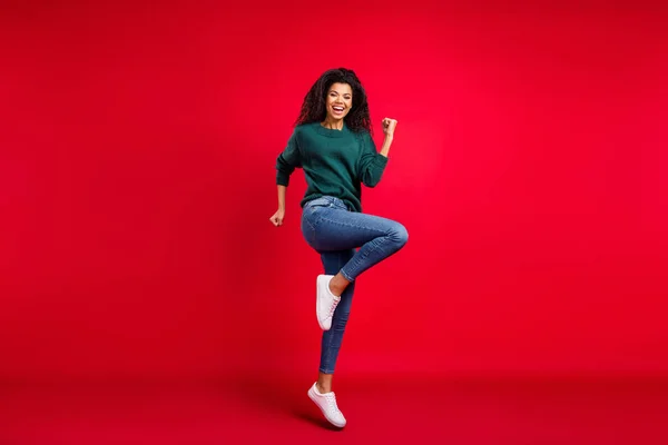 Foto de tamaño completo de la joven afro americana positiva ganadora buen humor aislado en el fondo de color rojo —  Fotos de Stock