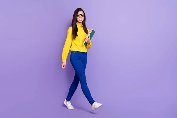 Фотографія повного тіла привабливої красивої молодої жінки, яка ходить коледж посмішка тримає нотатки ізольовані на фіолетовому кольоровому фоні — стокове фото