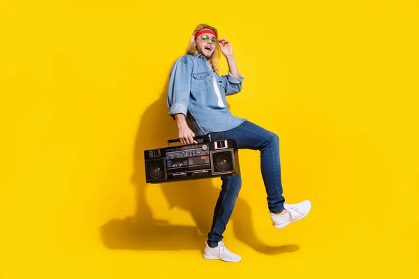 Φωτογραφία του αυτοπεποίθηση αστείο νεαρός ντυμένος πουκάμισο denim χαμογελώντας χορό κρατώντας boom κουτί απομονωμένο κίτρινο χρώμα φόντο — Φωτογραφία Αρχείου