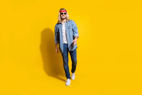 Foto de adorable atractivo joven caballero usar jeans camisa gafas oscuras caminando sonriente aislado color amarillo fondo —  Fotos de Stock