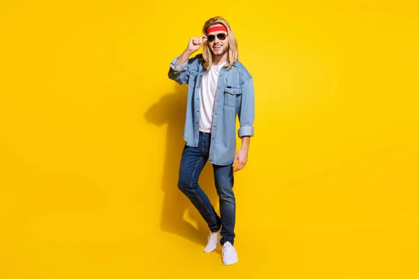 Foto de divertido caballero bastante joven usar jeans camisa gafas oscuras caminando sonriente aislado color amarillo fondo — Foto de Stock
