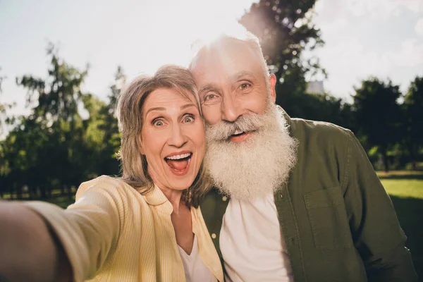 Foto de amigos jubilados divertidos positivos vestidos camisas casuales sonriendo virando selfie caminando al aire libre parque urbano de la ciudad —  Fotos de Stock