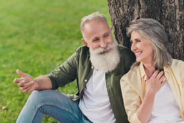Foto de alegre pareja jubilada de ensueño usan ropa casual caminando descansando sentados bajo el árbol hablando sonriendo fuera de la calle urbana de la ciudad — Foto de Stock