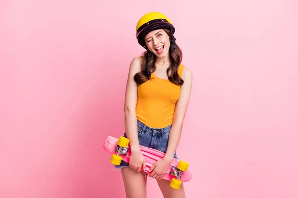 Foto de lindo millennial rizado peinado señora parpadeo ojo mantenga skate desgaste naranja top casco camisas aisladas en color rosa fondo —  Fotos de Stock