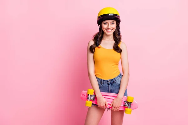 かわいい千年紀の波状の髪型の写真女性はピンクの色の背景に隔離されたオレンジトップヘルメットシャツを着用スケートを保持します — ストック写真
