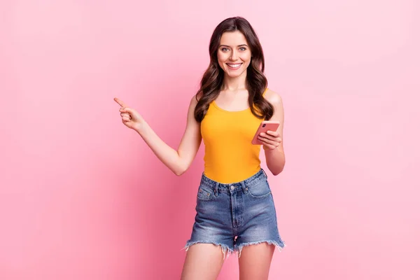 Foto de bonito encantador jovem mulher usar amarelo singlet leitura moderno gadget apontando espaço vazio isolado cor rosa fundo — Fotografia de Stock
