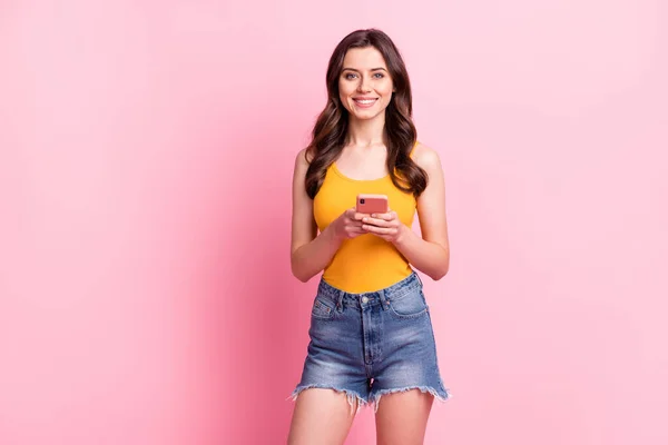 Foto de muito doce jovem senhora vestida amarelo tanque-top segurando dispositivo moderno sorrindo espaço vazio isolado cor de fundo rosa — Fotografia de Stock