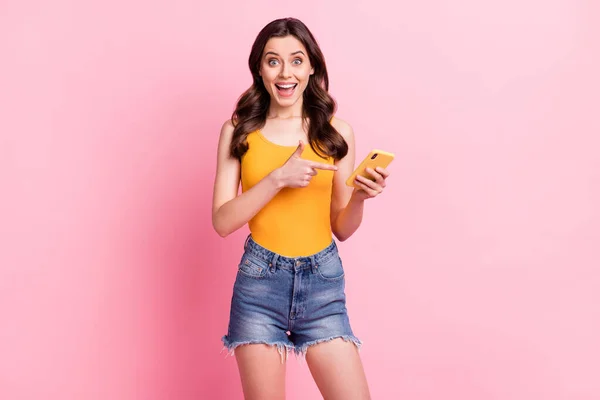 Foto de adorable impresionado joven mujer usar amarillo singlet sonriente dedo dedo moderno gadget aislado color rosa fondo — Foto de Stock