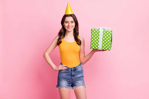 Photo of pretty adorable young woman wear yellow singlet birthday cone holding present box smiling isolated pink color background — Stock Photo, Image