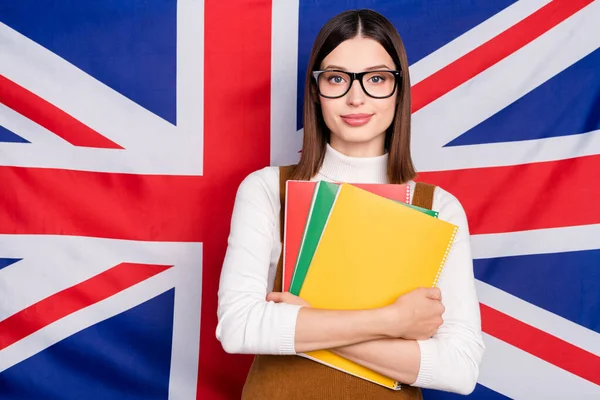 Foto de la joven niña bonita sostiene libro profesor gafas de idioma extranjero aislado sobre fondo de la bandera del Reino Unido —  Fotos de Stock