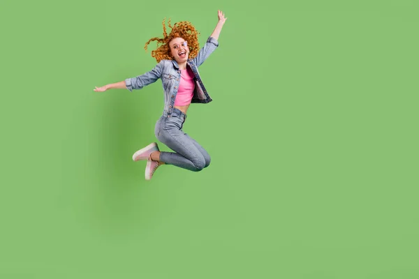Kot pantolon giyen, boş alandan atlayan, izole edilmiş yeşil arka planda gülümseyen güzel bir genç kadının uzun boylu fotoğrafı. — Stok fotoğraf