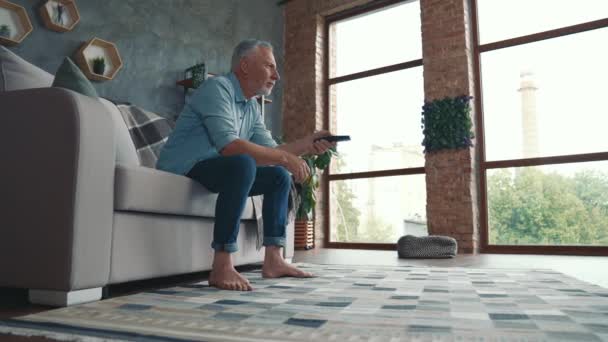 Мужчина средних лет сидит на диване и смотрит блокбастер в гостиной — стоковое видео
