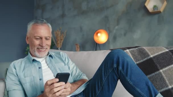 Bello uomo di mezza età sit divan uso dispositivo post commento in soggiorno — Video Stock