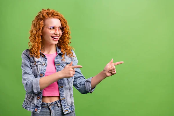 Photo of pretty cute young woman wear jeans outfit spectacles looking pointing fingers empty space smiling isolated green color background — Stock Photo, Image