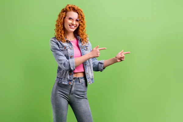 Foto di lucido bella giovane donna indossare jeans vestito occhiali puntando il dito vuoto spazio sorridente isolato colore verde sfondo — Foto Stock