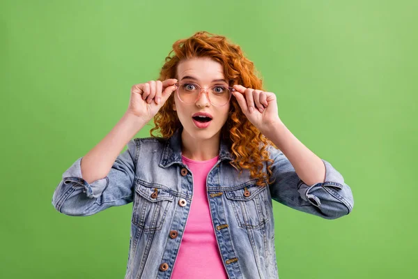 Fotografie mladé dívky ruce dotknout brýle ohromený pohled izolované přes zelené barvy pozadí — Stock fotografie