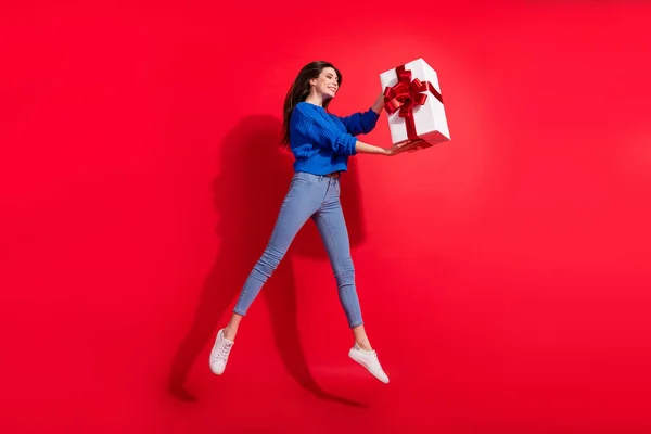 Pleine photo du corps de charmante jeune femme heureuse sauter tenir les mains boîte cadeau isolé sur fond de couleur rouge — Photo