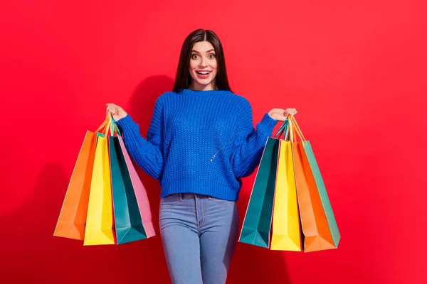 Foto van aantrekkelijke jonge charmante dame houd handen shopping tassen verbaasd geïsoleerd op rode kleur achtergrond — Stockfoto