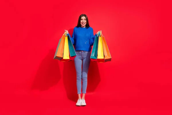 Full body foto van verbaasd blij opgewonden jonge vrouw houdt handen tassen klant geïsoleerd op rode kleur achtergrond — Stockfoto