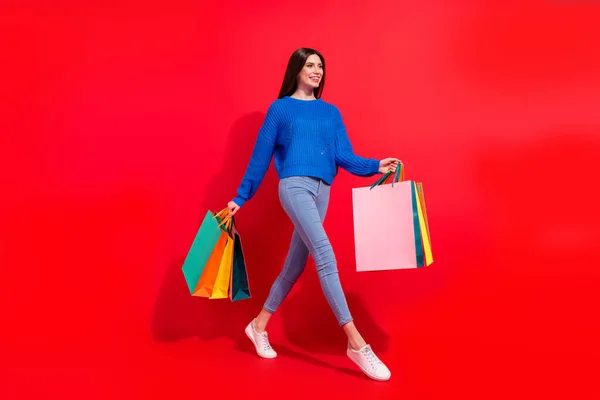Полноразмерная фотография профиля привлекательной счастливой молодой женщины на фоне пустого пространства магазина сумок, изолированного на красном фоне — стоковое фото