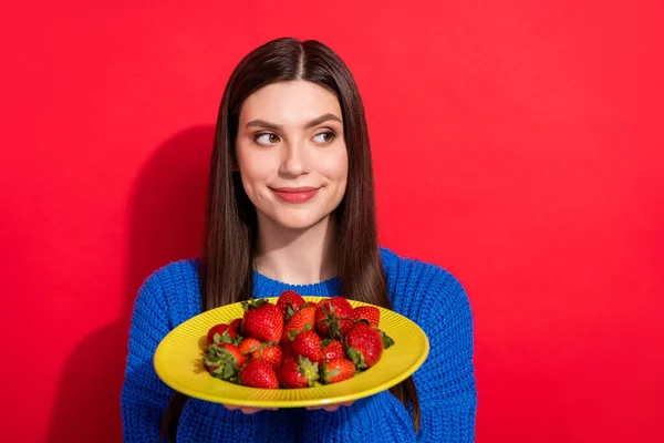 Foto de mujer joven encantadora mirada espacio vacío toma de la mano plato fresa aislado sobre fondo de color rojo —  Fotos de Stock