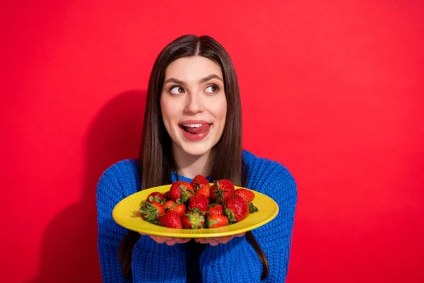 Фото мечтательной молодой женщины смотреть пустое пространство держать руки тарелку ягоды изолированы на красном фоне — стоковое фото
