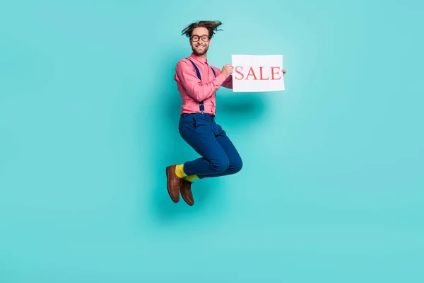 Foto de engraçado doce jovem vestido rosa camisa óculos segurando venda cartaz saltando alto isolado turquesa cor fundo — Fotografia de Stock