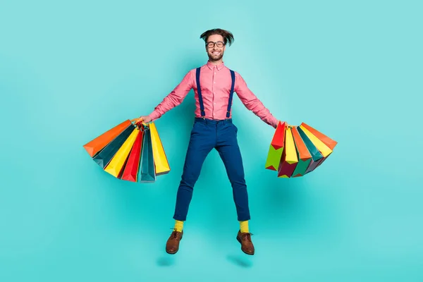 Foto van vrij grappige jonge man gekleed roze shirt bril houden boodschappentassen springen hoog geïsoleerde turquoise kleur achtergrond — Stockfoto
