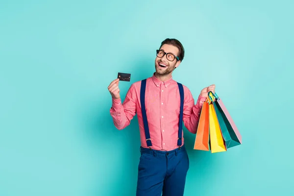 Photo of attractive dreamy guy dressed pink shirt spectacles holding bags card empty space isolated turquoise color background — 图库照片