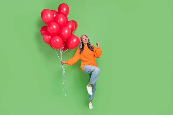 Beyaz saçlı yaşlı bayanın tüm vücut fotoğrafı bağırıyor. Balonlar, yeşil arka planda izole edilmiş kazak kotları giyiyor. — Stok fotoğraf