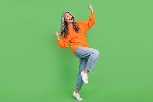 Full size photo of astonished white hair elder lady hands fists yell wear sweater jeans shoes isolated on green color background — Stock Photo, Image