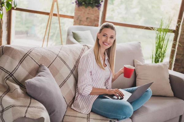 Foto de tamaño completo de la señora rubia joven linda escribir portátil beber ropa de té pantalones vaqueros camisa blanca en espacioso loft solo —  Fotos de Stock