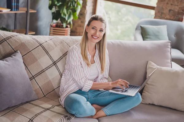 Full size foto van slimme jonge blonde dame zitten werken laptop dragen shirt jeans thuis in het weekend vakantie alleen — Stockfoto