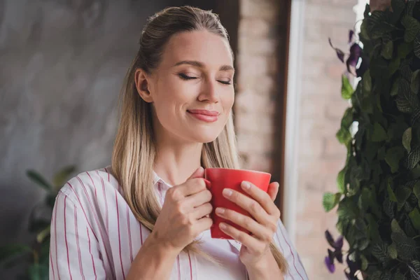 Foto van mooie volwassen blonde dame drinken thee dragen gestreept shirt thuis in ruime zolder alleen — Stockfoto