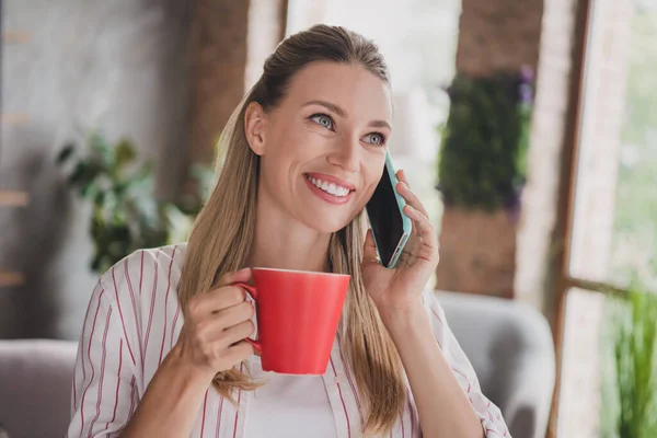 Photo of cute mature blond lady talk telephone drink wear striped shirt at home in spacious loft alone — Stock Photo, Image