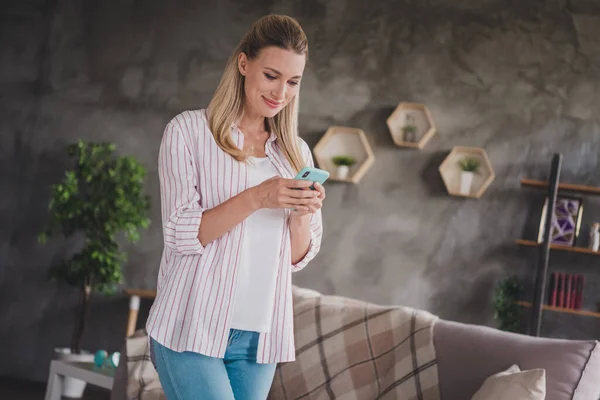 Фото красивой зрелой блондинки написать телефон носить полосатую рубашку самоизоляции дома в гостиной в одиночку — стоковое фото